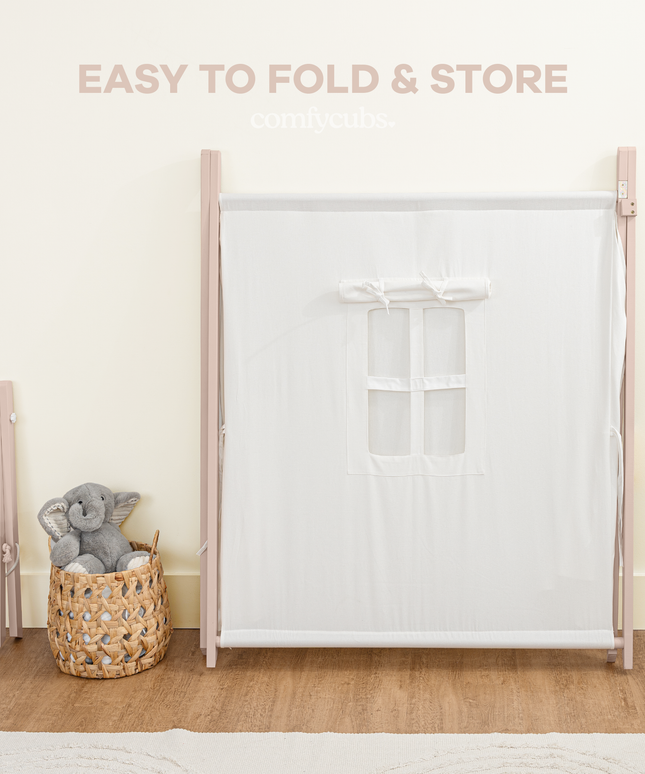 White tent with pink frame and mesh side panel, accompanied by a gray stuffed animal and wicker basket on a wooden floor.