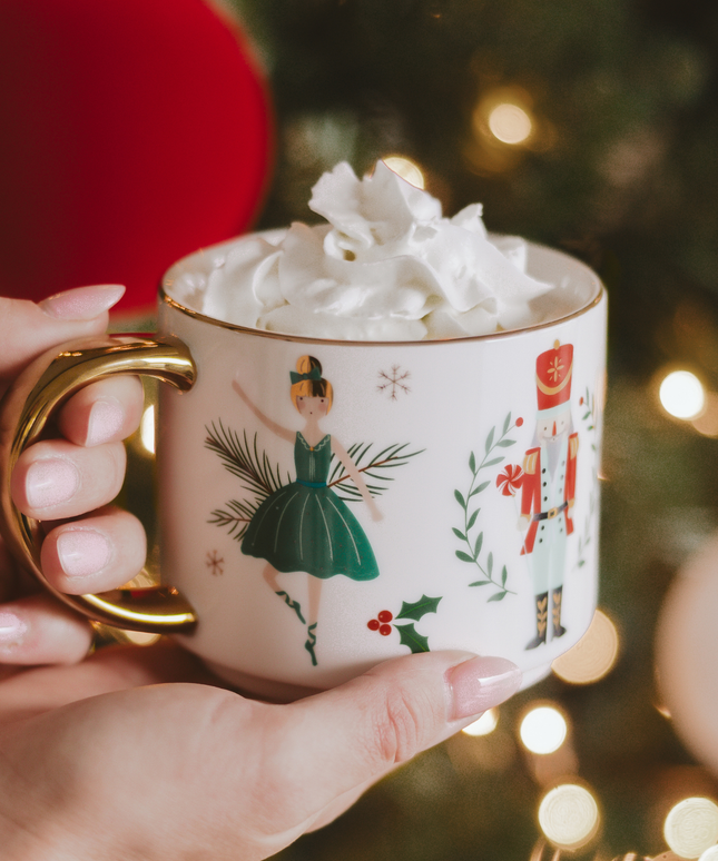 Hand holding a Christmas-themed mug with whipped cream against a festive background