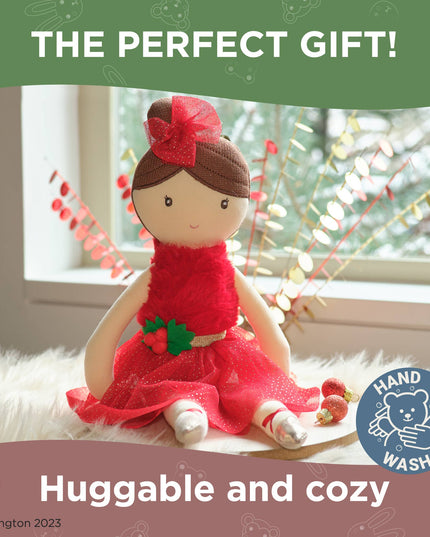Stuffed doll in a red dress with a flower on a soft surface, surrounded by festive decorations.