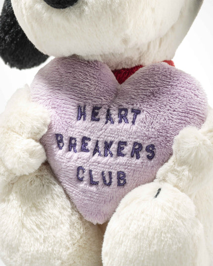 Stuffed dog holding a heart-shaped pillow with 'Heart Breakers Club' text on a white background