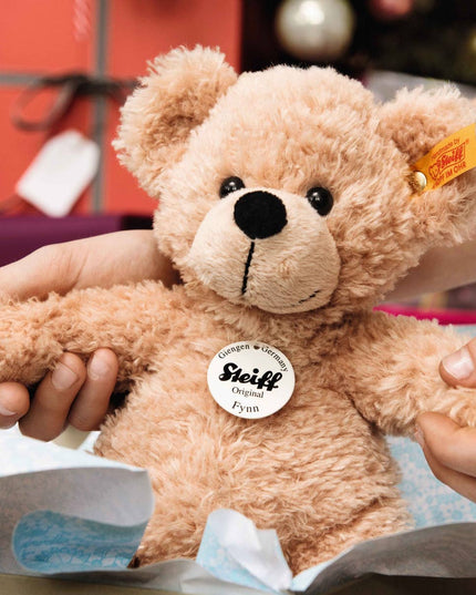 Person holding a Steiff teddy bear with a blurred festive background