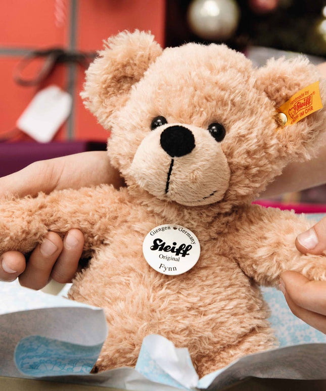 Person holding a Steiff teddy bear with a blurred festive background