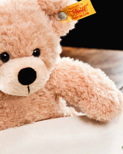 Plush teddy bear with a visible brand tag on a light surface.