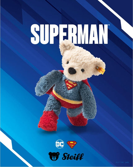 Plush teddy bear in Superman costume on a blue background with Steiff logo.
