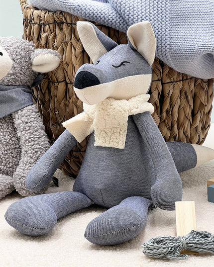 Gray plush toy with a scarf in a cozy setting with wicker basket and soft textures.