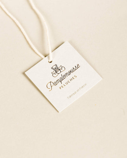 White tag with 'Pamplemousse Peluches' branding on a beige background