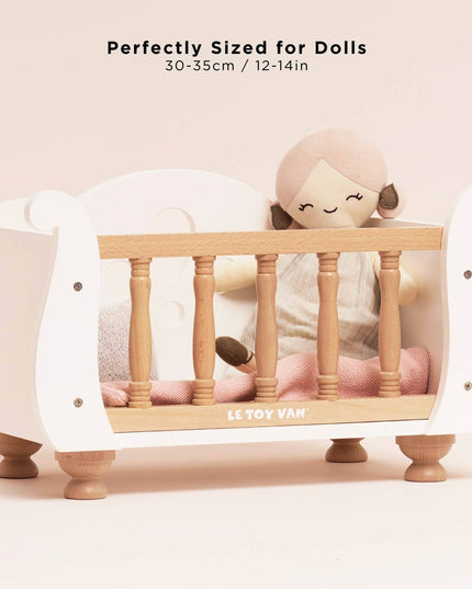 Small wooden crib with a doll inside, labeled 'LE TOY VAN', on a light pink background.