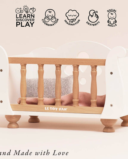 Wooden crib with white mattress and 'Le Toy Van' branding on a light pink background.
