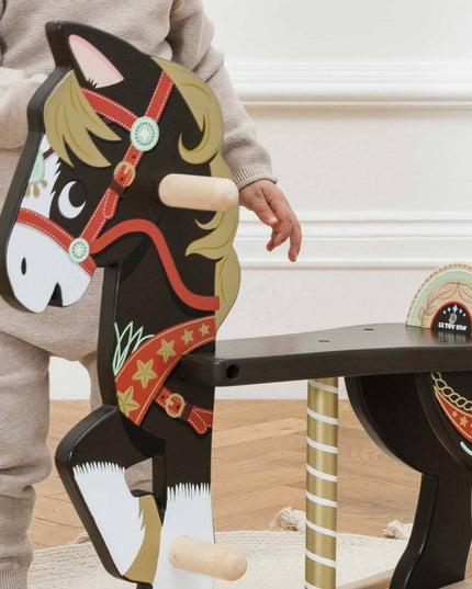 Child playing with a wooden horse toy on a wooden floor.
